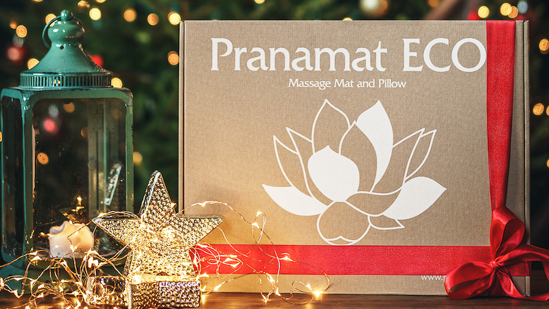 Pudełko z zestawem do masażu Pranamat ECO, przyozdobione świąteczną wstążką.